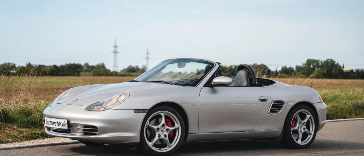 A silver Porsche Boxster S 986 with the top down parked on a coastal road