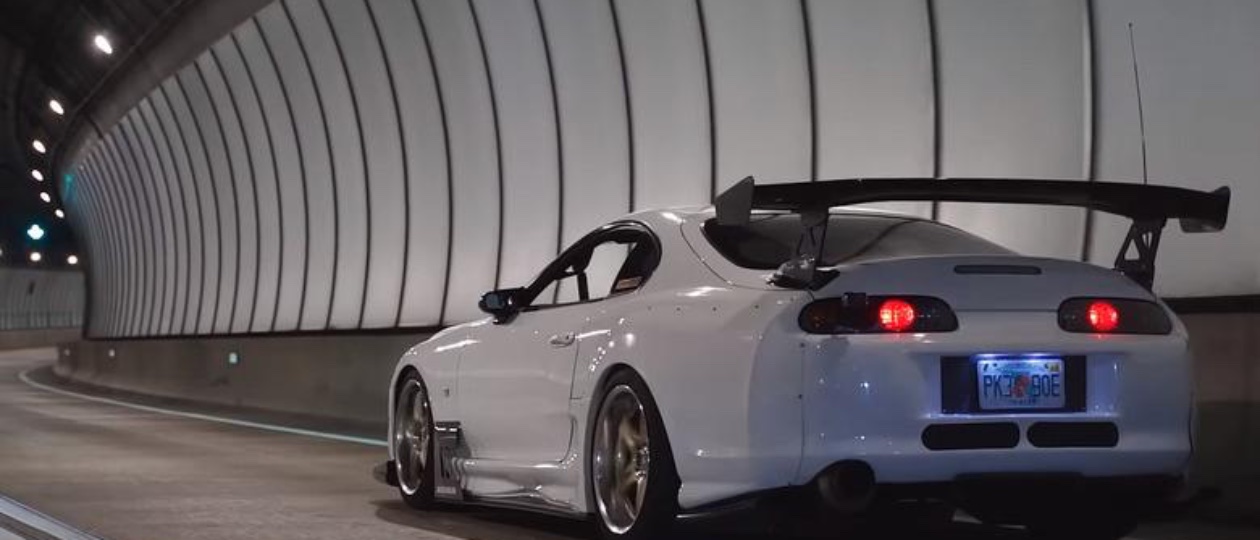 A super white Toyota Supra MK4 twin turbo with rear wing on an empty stretch of highway